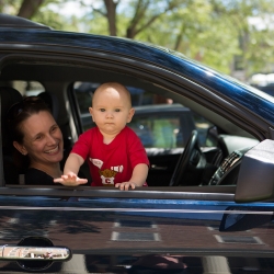 An adult holding a smiling child in the passenger seat of a car