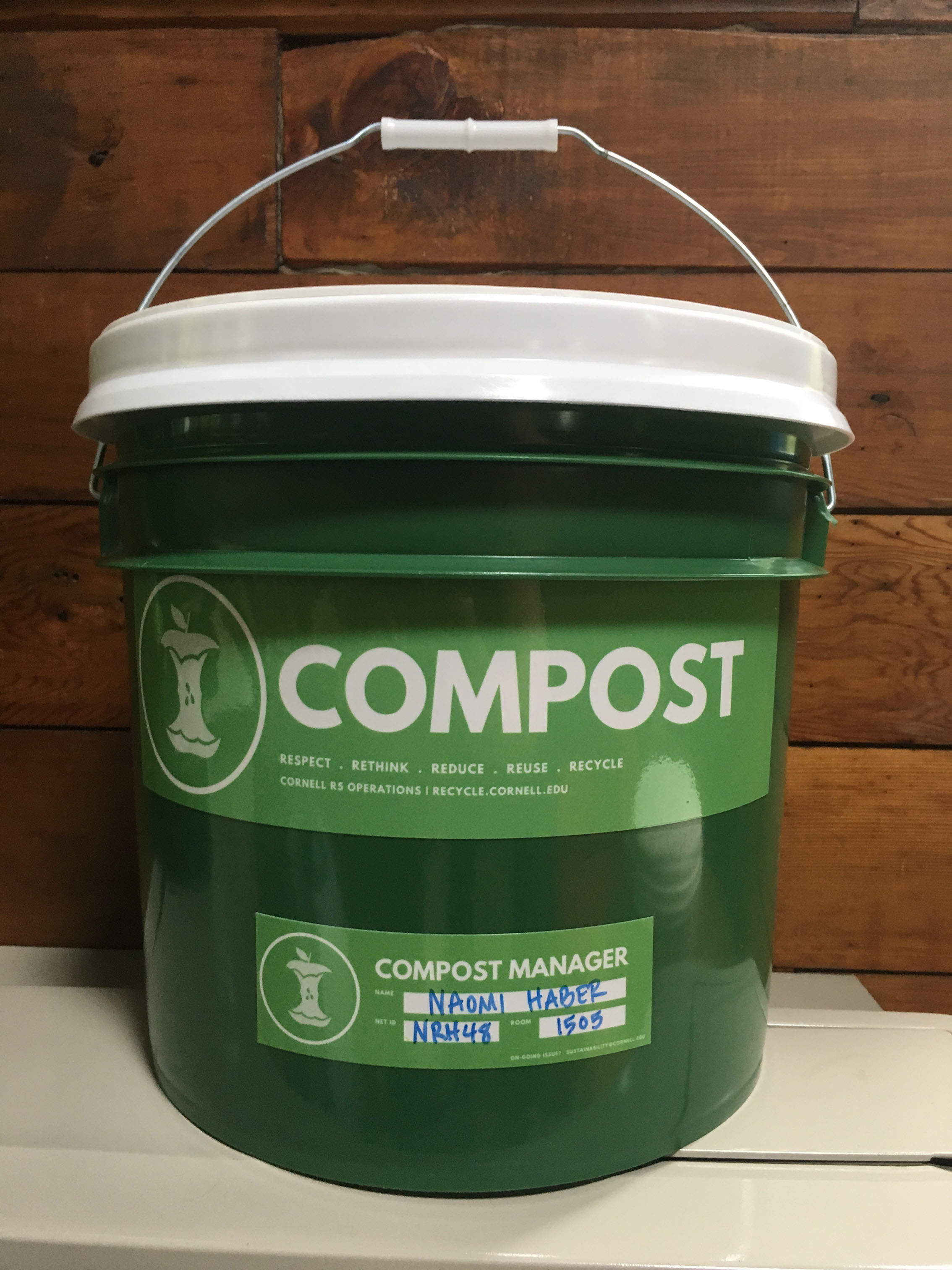Green residential compost bucket with text "Compost" and name of contact for that residential facility