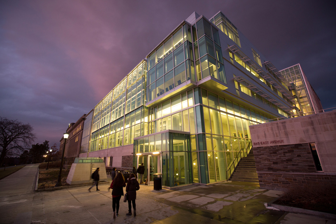 The glass facade of the Physical Sciences Building lit up in the evening.