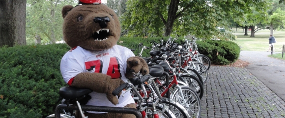 Big Red Bear stands next to a line of parked bikes on campus