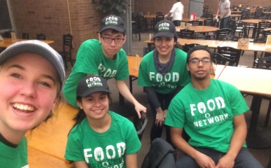 Five students wearing food recovery network shirts pose in a dining hall while reclaiming usable food