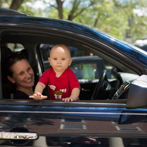 An adult holding a smiling child in the passenger seat of a car
