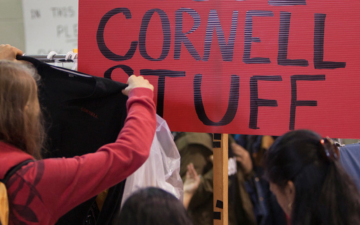 Student holds up a shirt before a sign reading "Cornell Stuff"
